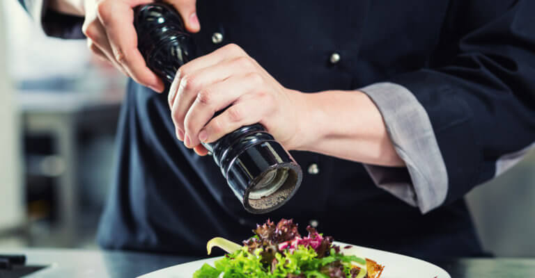 A chef adding some paper to a salad on a plate