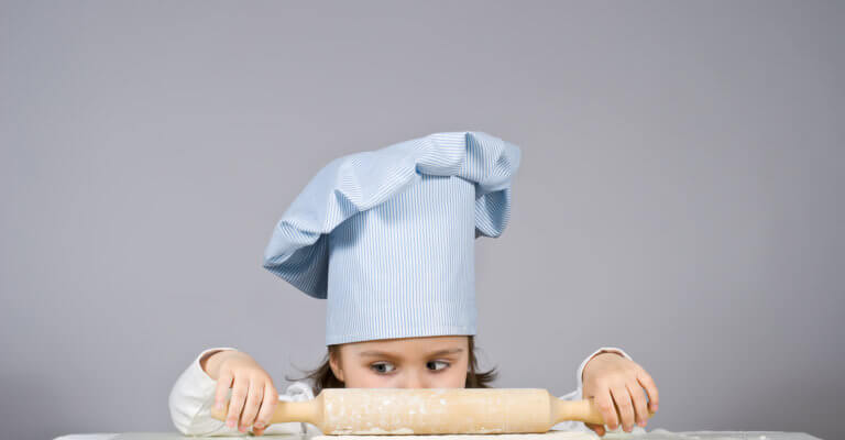 a child dressed as a chef using a rolling pin